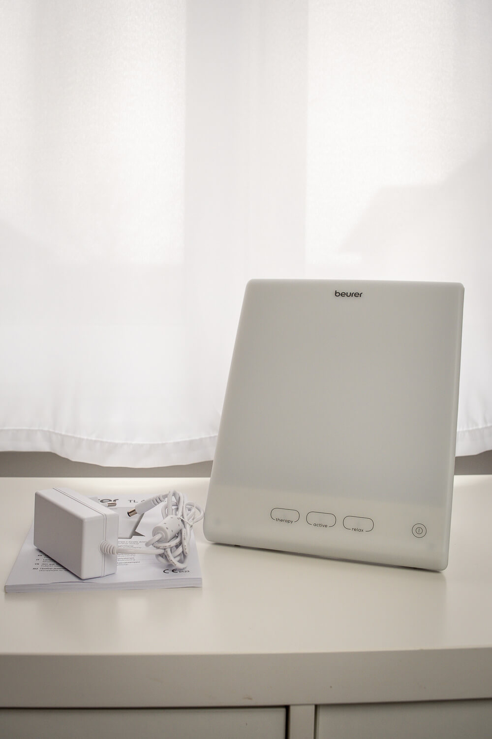 Contenu du coffret Beurer TL 45 : lampe de luminothérapie, adaptateur secteur et manuel d’utilisation posés sur une table.